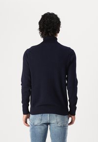 Marineblauer Pullover mit hohem Kragen, gerippten Bündchen und Saum, aus softem Stoff mit glatter Textur. Die Rückansicht zeigt klare Linien.