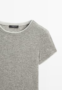 T-shirt in cotone grigio con maniche corte, collo a giro e una sottile trama. Presenta un bordo bianco a contrasto attorno al colletto. Etichetta del brand visibile.