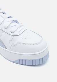 Valge nahkne tennisek, millel on helesinised aktsendid, lamedad paelad, perforeeritud varvas ventilatsiooni tagamiseks ning paks, tekstureeritud kummist tald.
