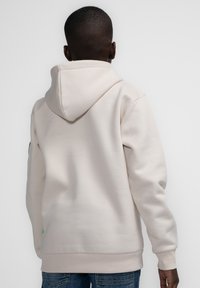 Lichtbeige hoodie gemaakt van zachte stof, met een kangaroozak, ribgebreide manchetten en een klein logo-accent nabij de zoom.