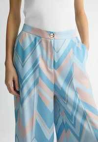 Leichte, gemusterte Hose in Blau und Pink mit einem Zickzackdesign. Verfügt über einen flachen Bund und ein dekoratives Knopfdetail.