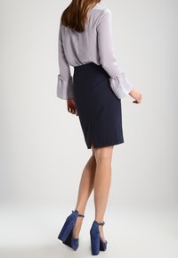 Ljuslila blus med trumpetärmar i kombination med en marinblå pennkjol med sprund bak. Avslutad med blå mocka klackskor med blockklack.