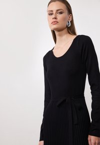 Schwarzes langärmliges Kleid mit passgenauer Oberseite und plissiertem Rock. Verfügt über einen Taillengürtel und eine glatte Textur, die eine elegante Silhouette schafft.
