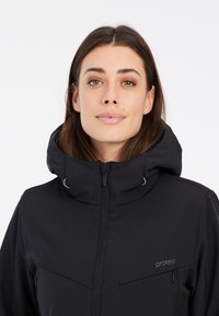 Schwarze Softshell-Jacke mit hohem Kragen, zentralem Reißverschluss und Logo. Verfügt über eine glatte Textur und dezente Einsätze für Stil.