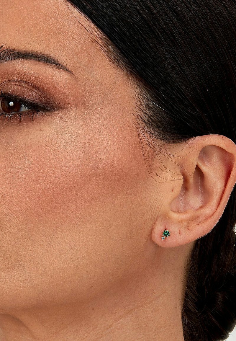 Boucles d'oreilles en émeraude avec de petits accents en diamant, montées en or, présentées sur l'oreille d'un modèle. Détails visibles sur la boucle d'oreille et la peau environnante.