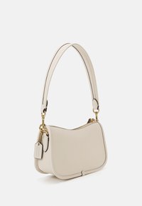 Sac à épaule en cuir crème avec une forme incurvée, quincaillerie en or et fermeture zippée. Il comporte une étiquette amovible et des accents de couture contrastante.