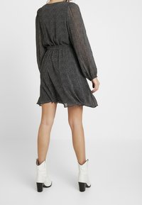 Svart plisserad klänning med långa, genomskinliga ärmar, smal midja och utställd kjol. Bärs med vita cowboystövlar och en hög blockklack.