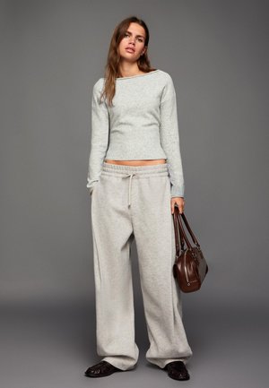 Világosszürke bordás pulóver hosszú ujjakkal laza, világosszürke melegítőnadrággal párosítva. Barna kézitáska dupla fogantyúval, texturált cipők.