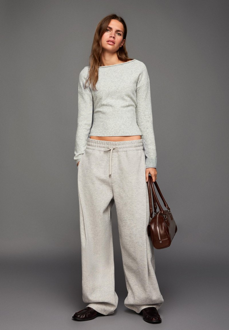 Jasnoszary prążkowany sweter z długimi rękawami w połączeniu z luźnymi, jasnoszarymi spodniami dresowymi. Brązowa torebka z podwójnymi uchwytami, teksturowane buty.