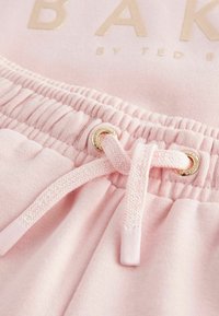 Pinke Baumwoll-Sweatpants verfügen über einen gerippten Bund und eine goldfarbene Metallöse mit passendem Kordelzug. Die Stofftextur ist weich.