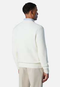 Cremfarbener Strickpullover mit gerippten Bündchen und Saum, der ein strukturiertes Muster aufweist. Über einem hellblauen Hemd mit Kragen getragen.