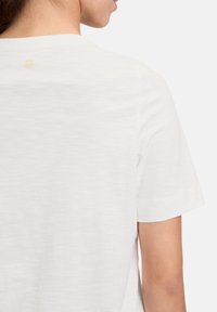Witte T-shirt met korte mouwen en een ronde hals, zachte textuur en een subtiele logodetail op de rug. Casual pasvorm en lichtgewicht stof.