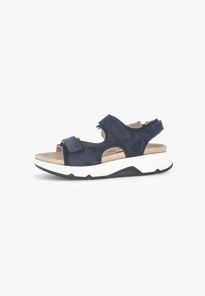 Sandales en suédine bleu marine avec des brides velcro, bout ouvert, semelle intérieure rembourrée beige et semelle en caoutchouc blanche épaisse avec des accents noirs.