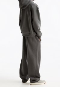 Mörkgrå hoodie och matchande vida sweatpants. Mjukt material, minimalistisk design, fickor på byxorna och något oversize-passform. Skorna är grå.
