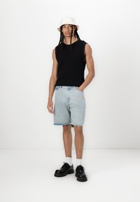 Black sleeveless knitted sweater, light blue denim shorts, black chunky shoes, and a beige bucket hat, set against a white background.