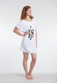 Valkoinen lyhythihainen mekko, jossa on värikäs geometrinen kuvio sinisessä, keltaisessa ja mustassa. Pehmeä kangas, rento malli ja polvimittainen design.
