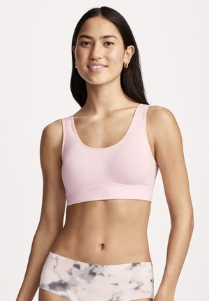 Young woman with long dark hair wears a light pink sports bra and high-waisted gray and white patterned leggings, smiling at the camera.