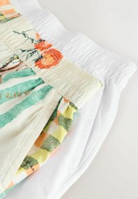Deux pantalons à taille élastique pliés, l'un blanc uni et l'autre avec un tissu imprimé rayé coloré et floral.