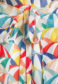 Kolorowa tkanina wzorzysta z przeplatającymi się kształtami w czerwonym, niebieskim, żółtym, zielonym i białym kolorze związaną kokardką pośrodku.