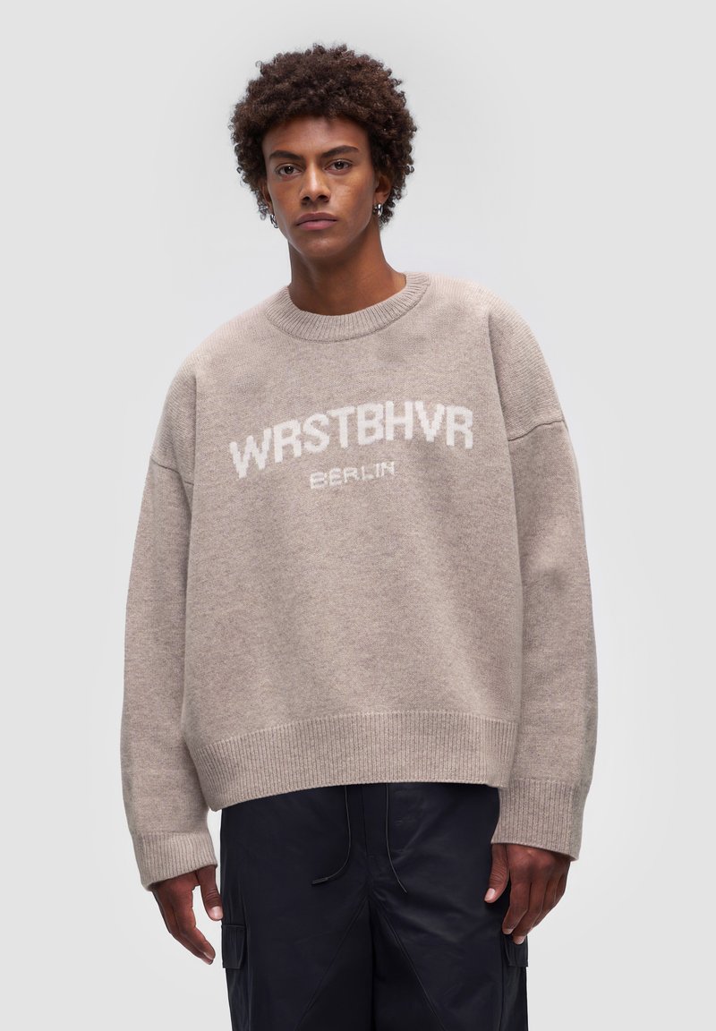 Beżowy, oversize sweter z miękkiego splotu, z białym logo "WRSTBHV" oraz "BERLIN" na klatce piersiowej, z prążkowanymi mankietami i dołem.