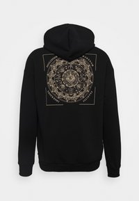Sweat à capuche noir avec un motif circulaire complexe présentant un œil au centre et les mots : désillusion, ennui, imprudent, ingénu.