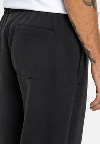 Czarne dresy wykonane z miękkiego materiału, z jednym tylnym kieszeniem, elastycznym paskiem w talii oraz luźnym krojem z detalami przeszycia.