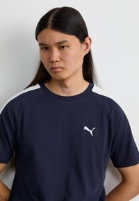 Mørkeblå T-shirt med hvide detaljer på skuldersømmene; har et lille hvidt Puma-logo på venstre bryst; glat bomuldsstof.
