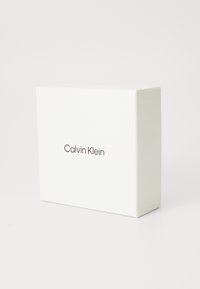 Witte vierkante doos met een gladde textuur, voorzien van de tekst "Calvin Klein" in een eenvoudige zwarte lettertype aan de voorkant.