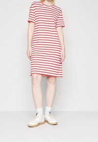 Personne portant une robe mi-longue à rayures horizontales blanches et rouges, des chaussettes blanches et des baskets blanches avec des semelles beiges.