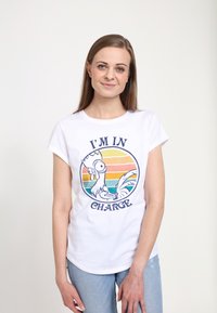 Hvid bomulds t-shirt med en grafik af en tegneseriehaner, der bærer en krone, med teksten "JEG ER ANSVARLIG," sat mod en stribet solnedgangsbaggrund.