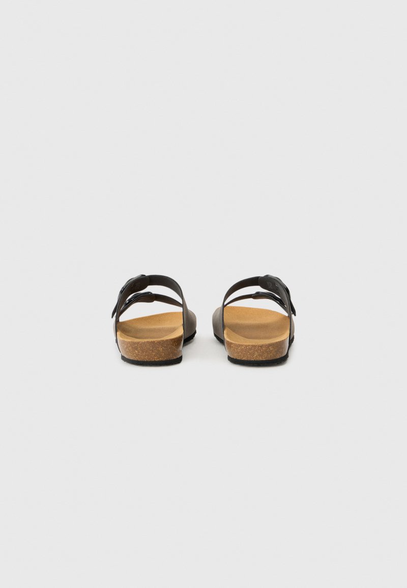Une paire de sandales en cuir noir avec des semelles en liège et des sangles ajustables, montrée de dos sur une surface blanche uniforme.