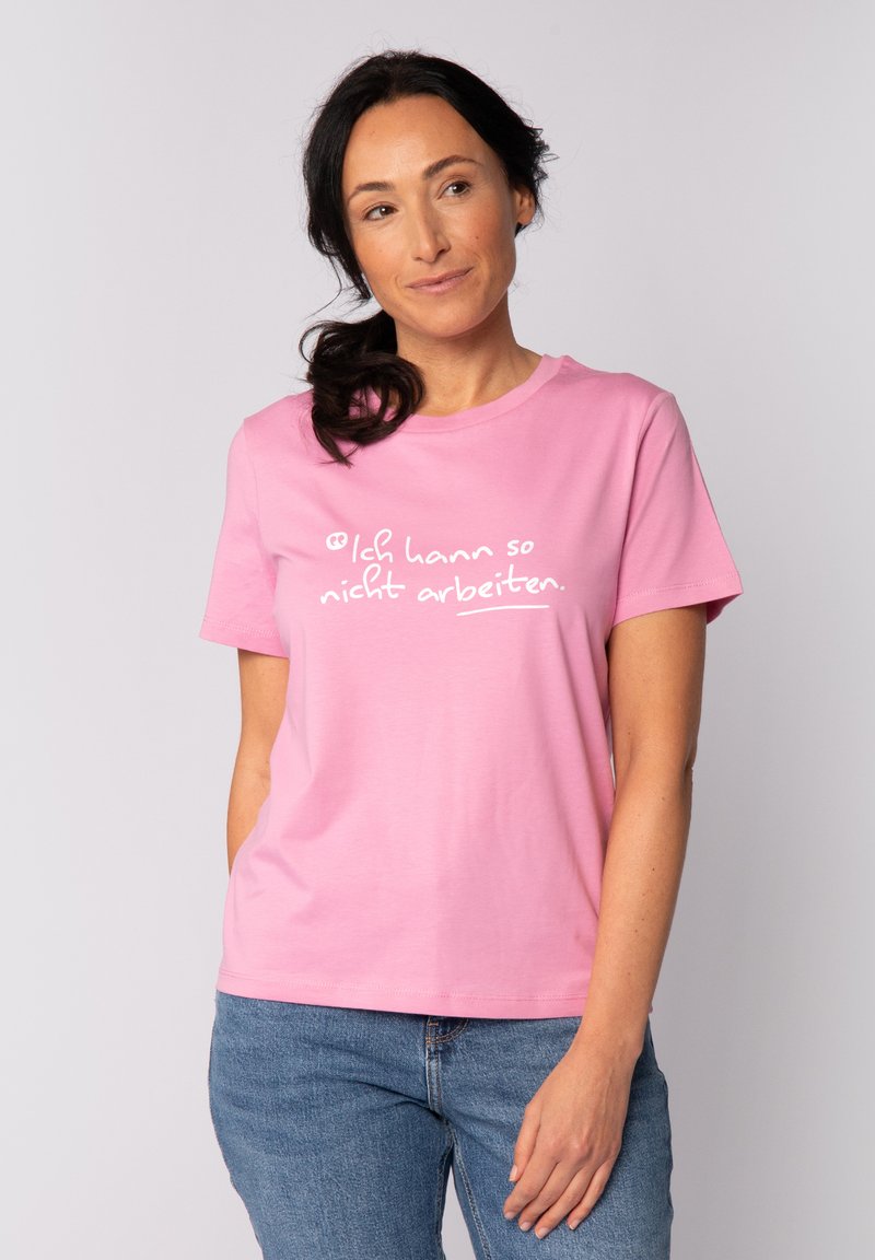 T-shirt en coton rose avec un col rond, des manches courtes et un texte imprimé blanc sur le devant. Associée à un jean en denim bleu.