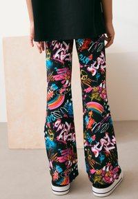 Färgglada utsvängda byxor med en svart bas och livliga mönster i graffiti-stil i rosa, blått, gult och orange. Material i bomullsblandning.
