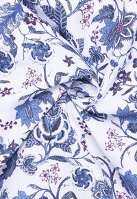 Witte stof met complexe bloemmotieven in blauw, paars en zwart, met een gestructureerde uitstraling, die verschillende bloemen- en bladontwerpen laat zien.