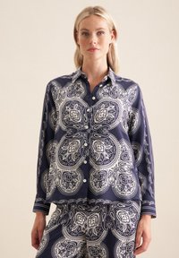 Completo pigiama blu navy con motivo paisley bianco, composto da una camicia con colletto e chiusura a bottoni, e pantaloni coordinati con lo stesso motivo.