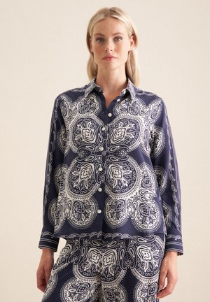 Completo pigiama blu navy con motivo paisley bianco, composto da una camicia con colletto e chiusura a bottoni, e pantaloni coordinati con lo stesso motivo.