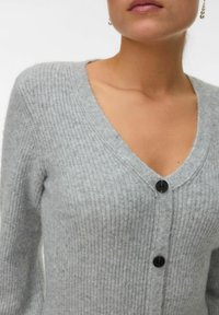 Cardigan grigio lavorato a maglia con scollo a V, maniche lunghe e bottoni neri. La texture è morbida con un motivo a coste.