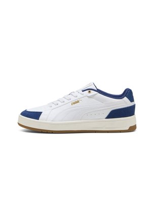 Baskets basses blanches Puma avec des touches bleu marine au talon et à l’orteil, semelle crème, et logo Puma doré sur le côté.