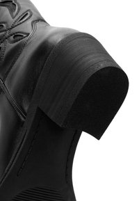 Bota de cuero negro con costuras intrincadas, tacón redondeado y suela texturizada. Enfoque en materiales duraderos y un diseño estructurado.