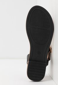 Musta sandaalin pohja, jossa on uurrettu kuvio, vaaleanruskeat yksityiskohdat ja kokomerkintä 37. Sivussa on sileä, kaartuva muotoilu.