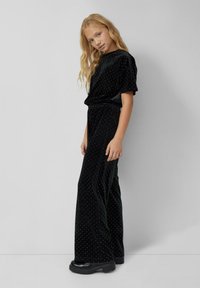 Zwart fluwelen outfit bestaande uit een kort mouwtop en wijde broek met witte stippen, ontworpen met een elastische tailleband.