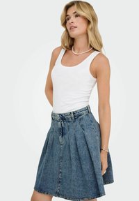 Jupe en denim avec des plis, mi-longue, délavée bleue, taille ceinturée, associée à un débardeur blanc ajusté. Texture lisse, style décontracté.