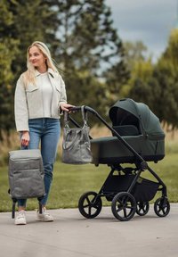 Kočárek s tmavě zelenou látkou, černým rámem a čtyřmi koly. Součástí je šedý batoh a kabelka s popruhy. Městské venkovní prostředí.