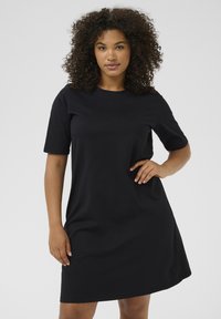 Vestido negro de manga corta hecho de una tela suave, con cuello redondo, corte holgado y largo hasta la rodilla. Diseño liso sin patrones.
