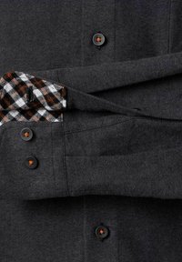 Graues Flanellhemd mit schwarzen Knöpfen. Die Ärmelaufschläge zeigen ein kontrastierendes schwarz-weißes Karomuster mit orangefarbenen Akzenten.