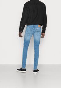 Svetle modré skinny džíny s vybledlým designem, pět kapsami a hnědou koženou nášivkou na zadní straně. Kombinované s černou dlouhým rukávem.