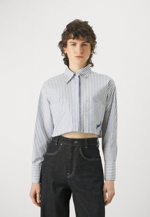 Camicia a righe blu e bianche tagliata, con maniche lunghe, colletto a bottoni, due tasche frontali e dettagli ricamati sull'orlo.