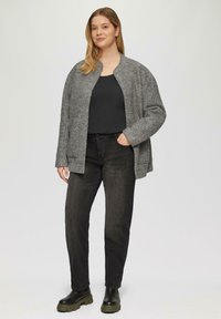Grijze wolmix cardigan met een eenvoudige ronde hals, zijzakken en een losse pasvorm, gecombineerd met zwarte jeans en stevige zwarte laarzen.