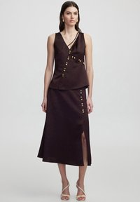 Dark purple two-piece outfit featuring a sleeveless top with a wrap design and decorative buttons, paired with a high-slit skirt.