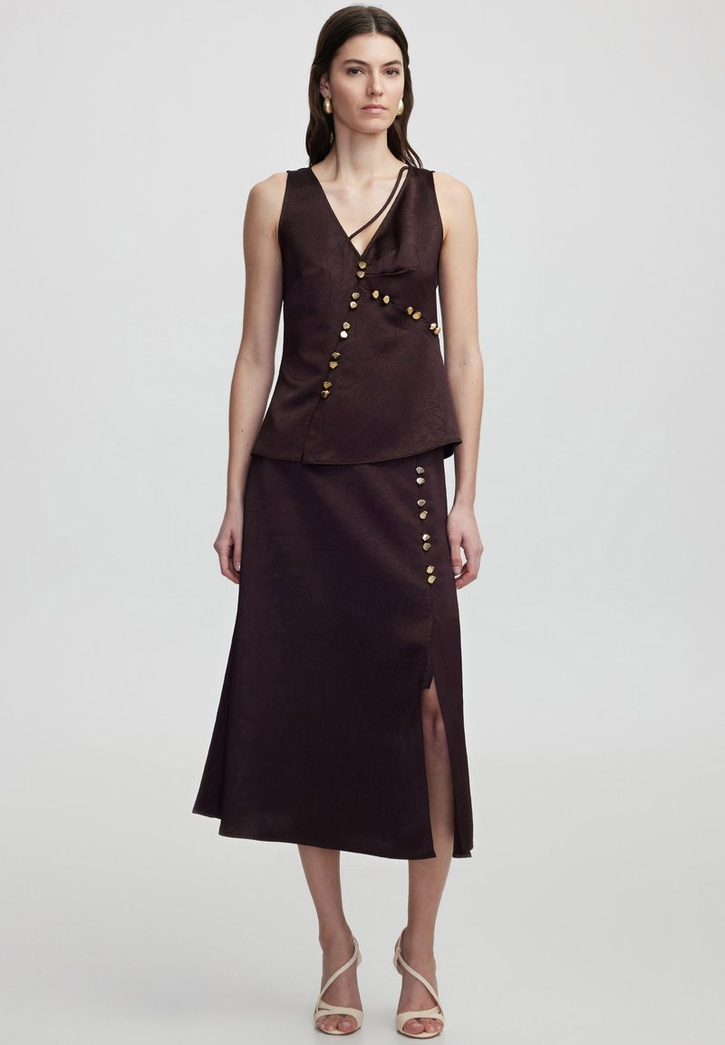 Dark purple two-piece outfit featuring a sleeveless top with a wrap design and decorative buttons, paired with a high-slit skirt.